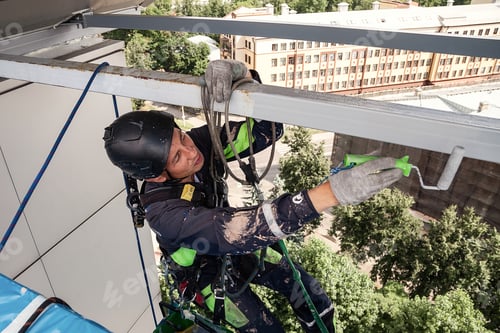 Preview: Industrial mountaineering worker in uniform hangs over building and paint roller