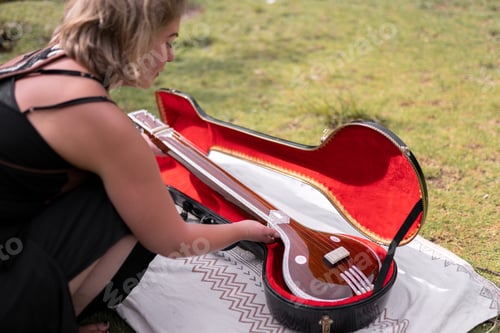 Preview: A young adult woman is picking up her indian tanpura suitcase in the nature