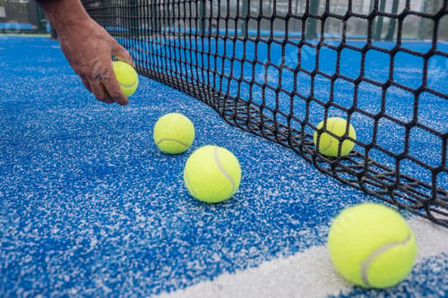 Preview: Close-up of a hand picking up tennis balls from a blue court near the net.