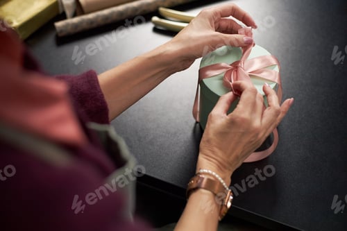 Preview: Middle Aged Caucasian Woman Decorating Gift Box with Pink Ribbon for Flowers