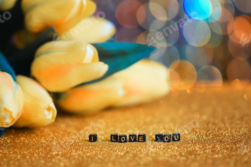Preview: I love you. The inscription is laid out in letters on a gold background. Yellow flowers. bokeh.