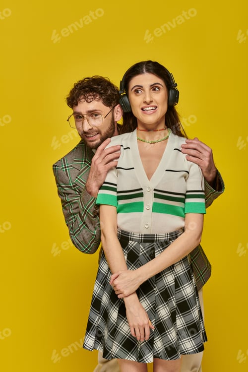 Preview: happy woman in wireless headphones listening music near bearded man, funny students, yellow backdrop
