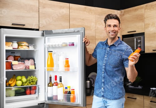 Preview: Man with bottle of juice near refrigerator in kitchen