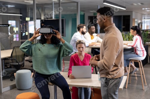 Preview: Hispanic businesswoman discussing with african american businesswoman wearing vr headset in meeting