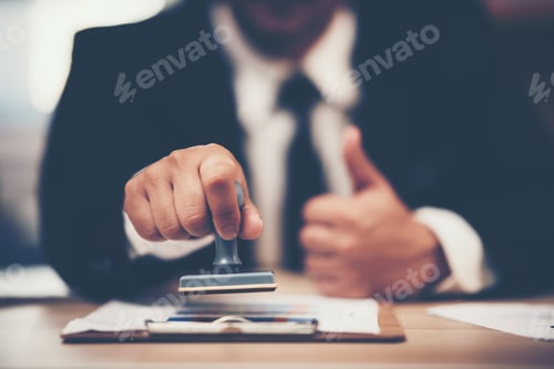 Preview: Close-up Of A Person's Hand Stamping With Approved Stamp On Document At Desk