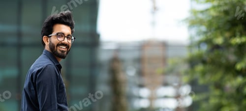 Preview: Cheerful handsome young indian guy posing by business center