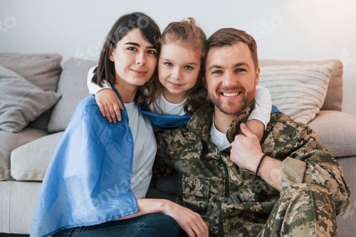 Preview: Ukrainian flag is on the shoulders. Soldier in uniform is at home with his wife and daughter