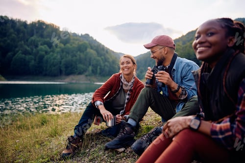 Preview: Group of young happy friends relaxing by the lake in nature.