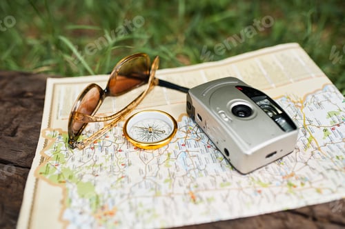 Preview: Close-up photo of compass laying on the map next to the camera and sunglasses.