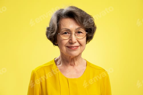 Preview: Attractive 70s woman wearing eyeglasses and casual yellow blouse, isolated on yellow background
