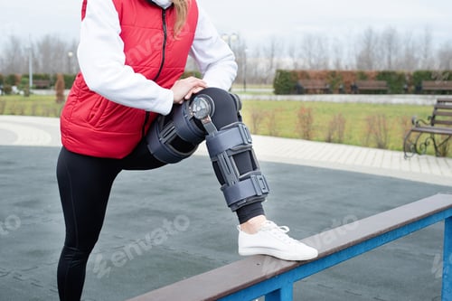 Preview: Woman wearing knee brace or orthosis after leg surgery working out in the park