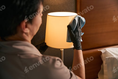 Preview: Chambermaid in gloved hands doing dusting in hotel room