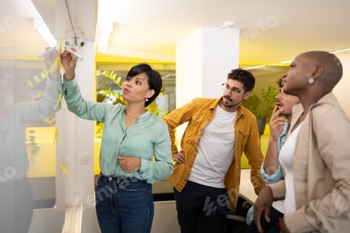 Preview: Happy diverse team members at writing board with woman manager sticking notes