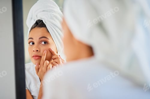 Preview: Shot of an attractive young woman squeezing a pimple on her face in the bathroom