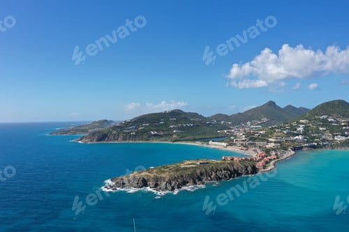 Preview: Aerial view of a coastal town with clear blue waters, mountains, and scattered clouds