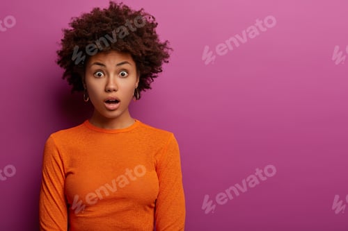 Preview: Indoor shot of shocked curly haired woman horrified to find out about awful accident, dressed in ora