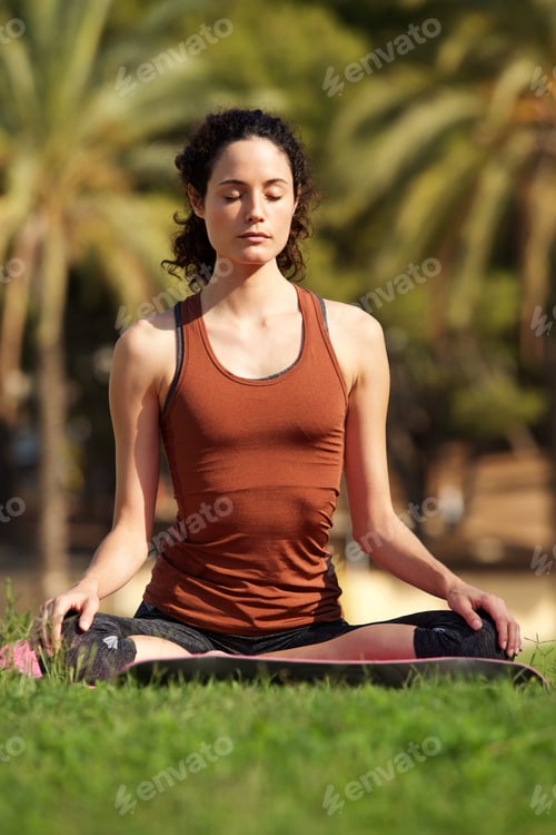 Preview: young woman sitting in lotus position doing yoga in park