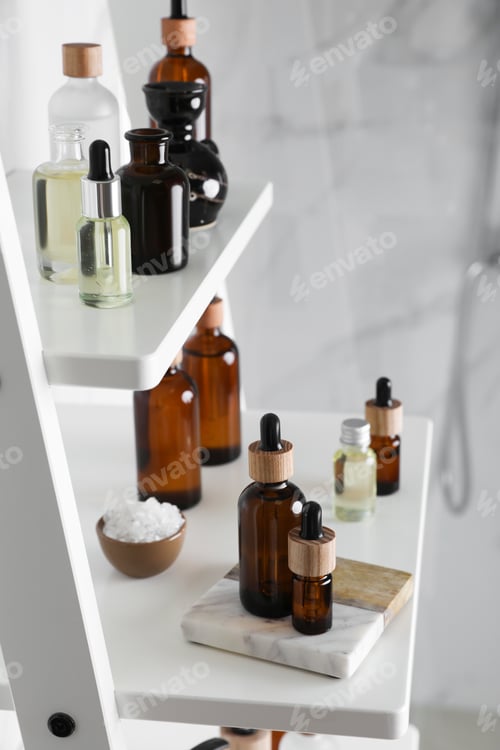 Preview: Essential oils, sea salt, and other cosmetic products on white shelving unit in bathroom