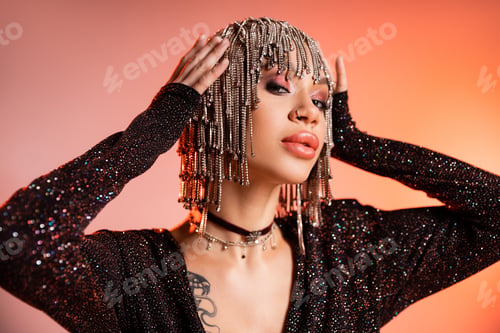 Preview: portrait of tattooed woman in black lurex dress touching wig with shiny rhinestones on coral pink
