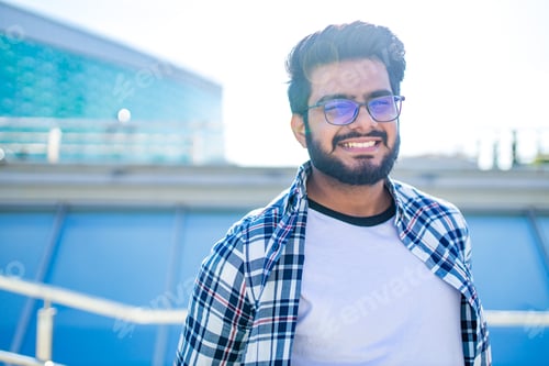 Preview: arabian young man in stylish checkered shirt and white t-shirt in downtown at summer day
