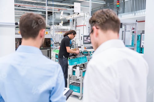 Preview: Two businessmen in factory shop floor with man in background working