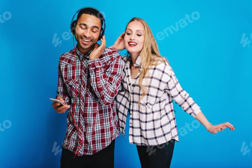 Preview: Joyful handsome man listening to music in headphones with closed eyes on blue background. Pretty you