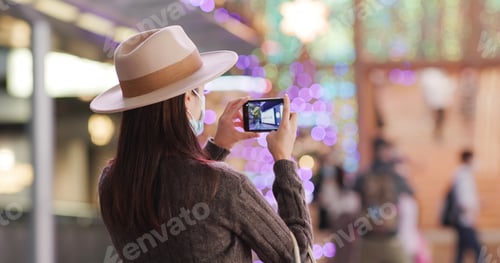 Preview: Woman use cellphone to take photo of the Christmas decoration in city at night