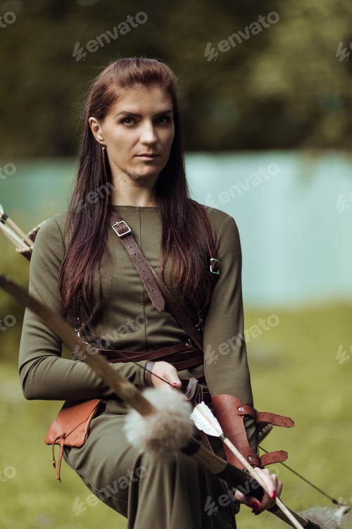 Preview: Portrait of a woman in a medieval costume with arrows and a bow on a blurred background, close-up