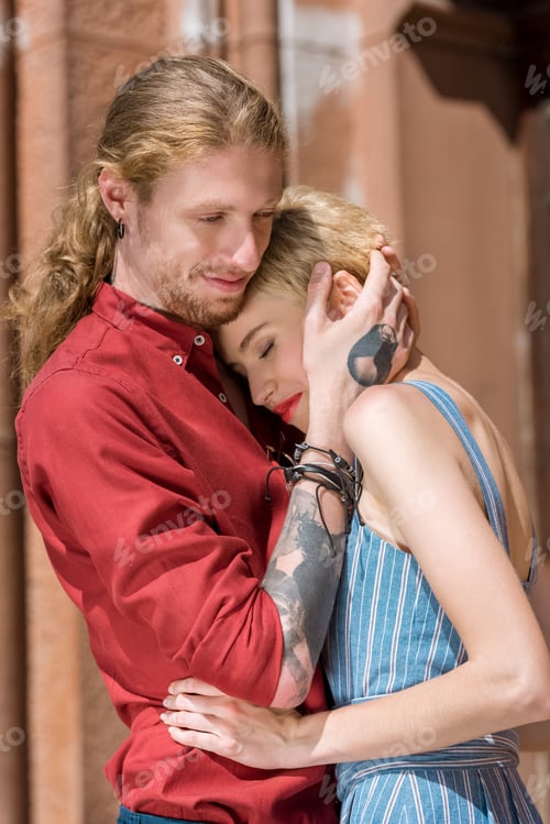 Preview: happy boyfriend with tattoos and stylish girlfriend cuddling on street