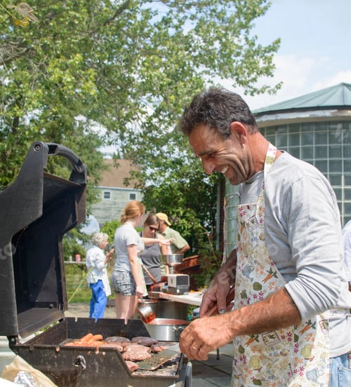 Preview: Side view of mature man cooking for family on barbecue looking down smiling