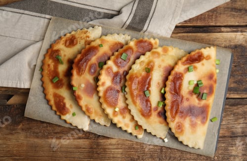 Preview: Board with delicious fried chebureki on wooden table, flat lay