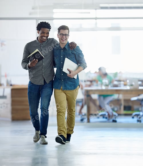 Preview: Shot of a two young coworkers talking together while walking arm in arm through their office