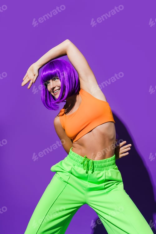 Preview: Carefree woman dancer wearing colorful sportswear having fun against purple background