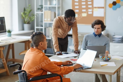 Preview: Portrait of black young woman with disability working in IT development company and using laptop
