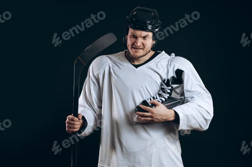 Preview: Confident hockey player looking at camera with skate in hand. Isolated on black.