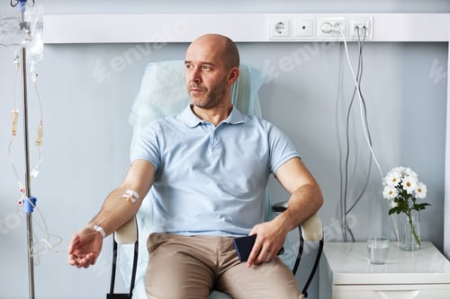 Preview: Adult man sitting in chair with IV drip during treatment session in clinic