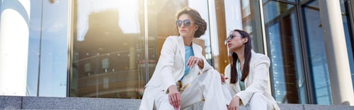 Preview: Female friends in trendy outfits relaxing in a city sitting on stairs