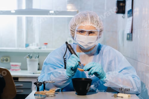 Preview: A dental technician in protective clothing is working on a prosthetic tooth in his laboratory