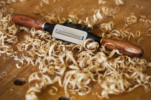 Preview: A traditional spokeshave with smooth wooden handles on wood covered with fresh curled wood shavings.