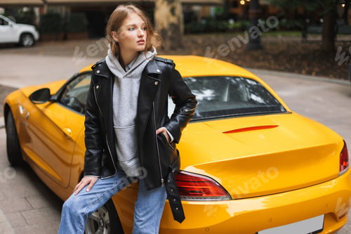 Preview: Young beautiful woman in leather jacket leaning on yellow sport