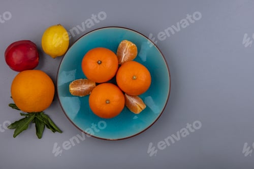 Preview: top view oranges with peeled wedges on a blue plate with peach and lemon on a gray background