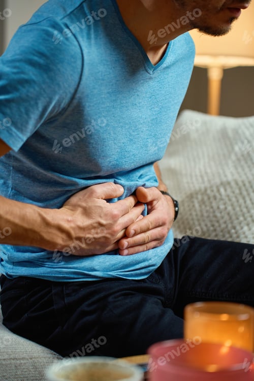 Preview: Man holding stomach while sitting on sofa at home