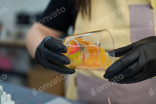 Preview: Candle maker adding colorful wax to glass jar in workshop