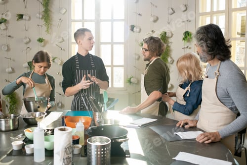 Preview: Contemporary young and mature people in aprons looking at male cooking coach