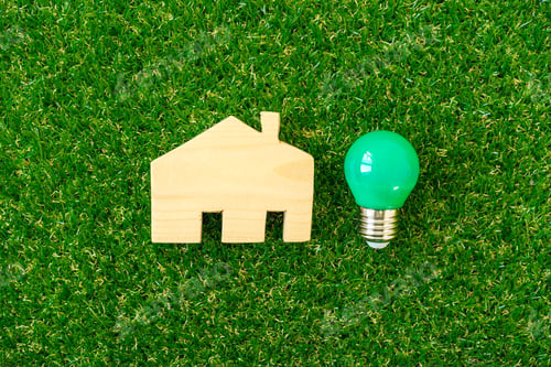 Preview: Wooden house model and lightbulb on green background