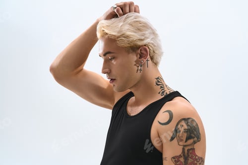 Preview: Stylish young man with tattoos showcases modern fashion in a minimalist setting
