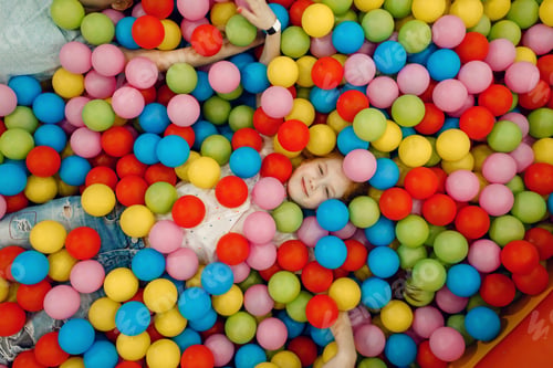 Preview: Girl lying among many colorful balls, playground