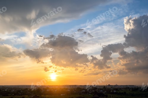 Preview: Dramatic sunset landscape of rural area with puffy clouds lit by orange setting sun and blue sky.