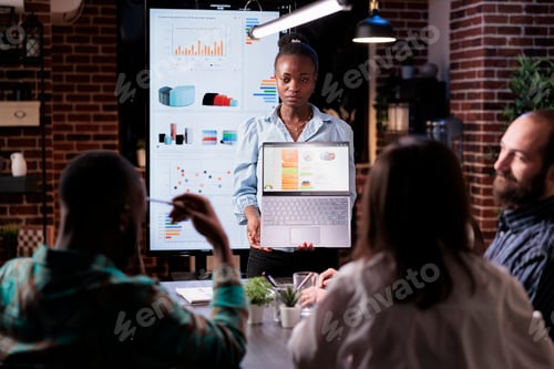 Preview: African american woman standing in business office presenting business analytics on laptop screen