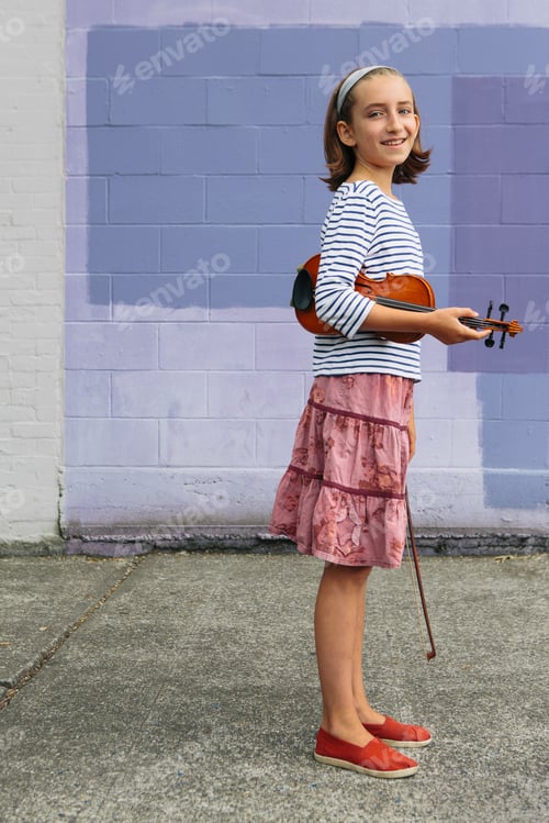 Preview: A ten year old girl holding a violin under her arm and a bow in her hand.